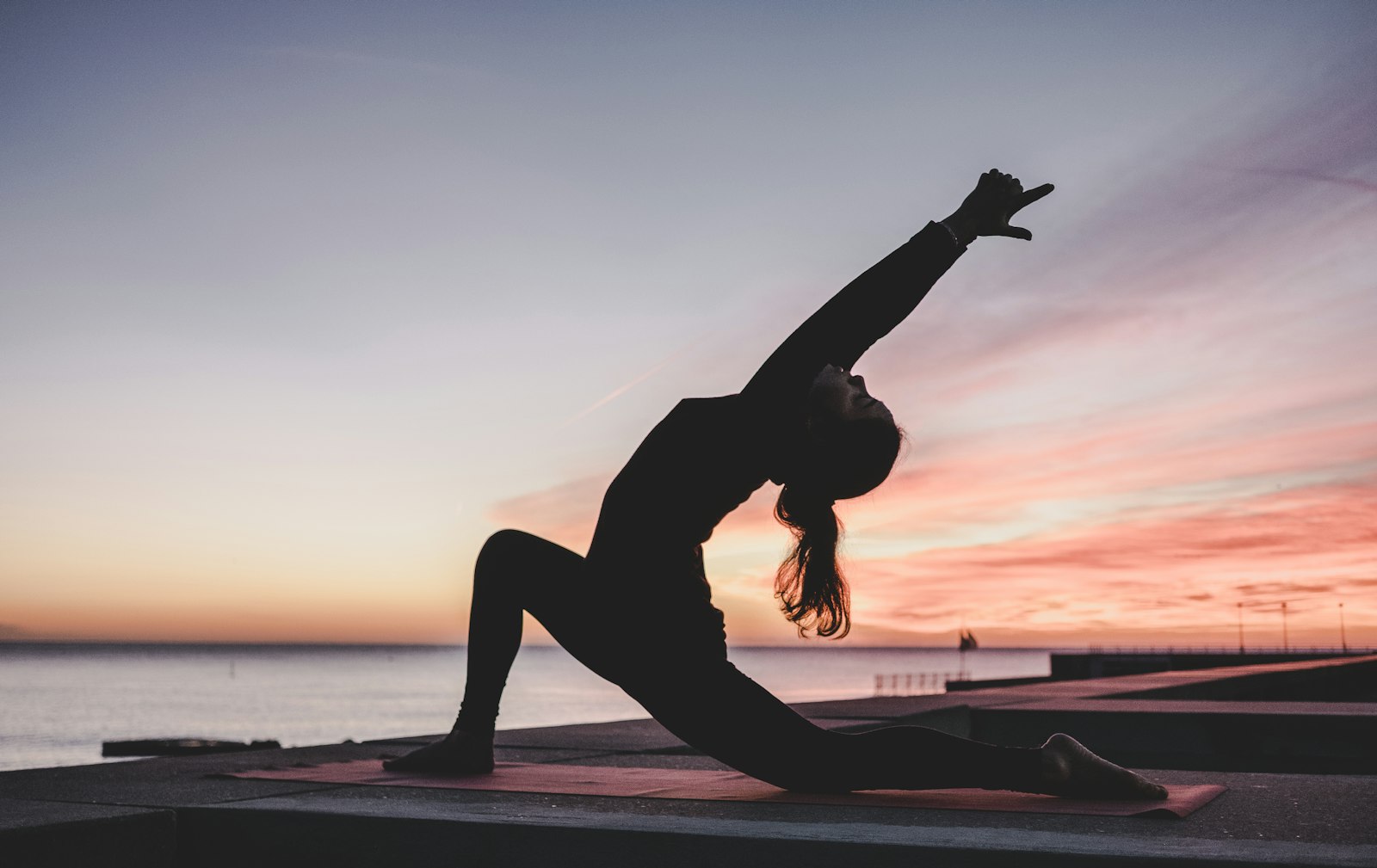 A woman practicing yoga at sunset beside the water